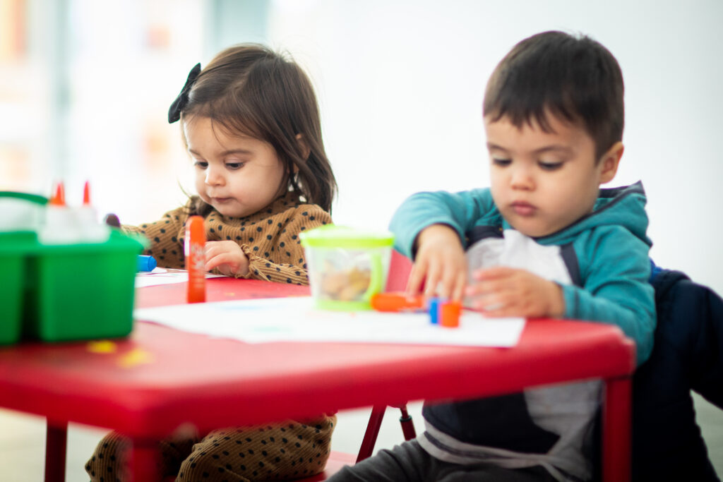 Two toddlers look down at a table while working on an art project